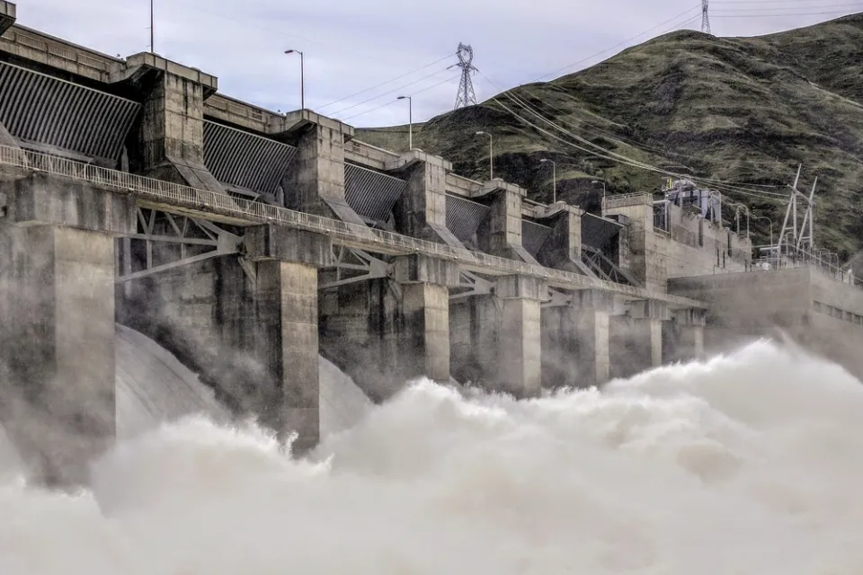 Water rushes over a spillway at a large concrete dam.